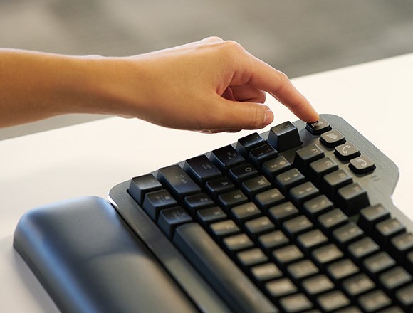 Person's finger pressing customizable meeting control buttons on Kensington's MK7500F Silent mechanical keyboard with wrist rest.